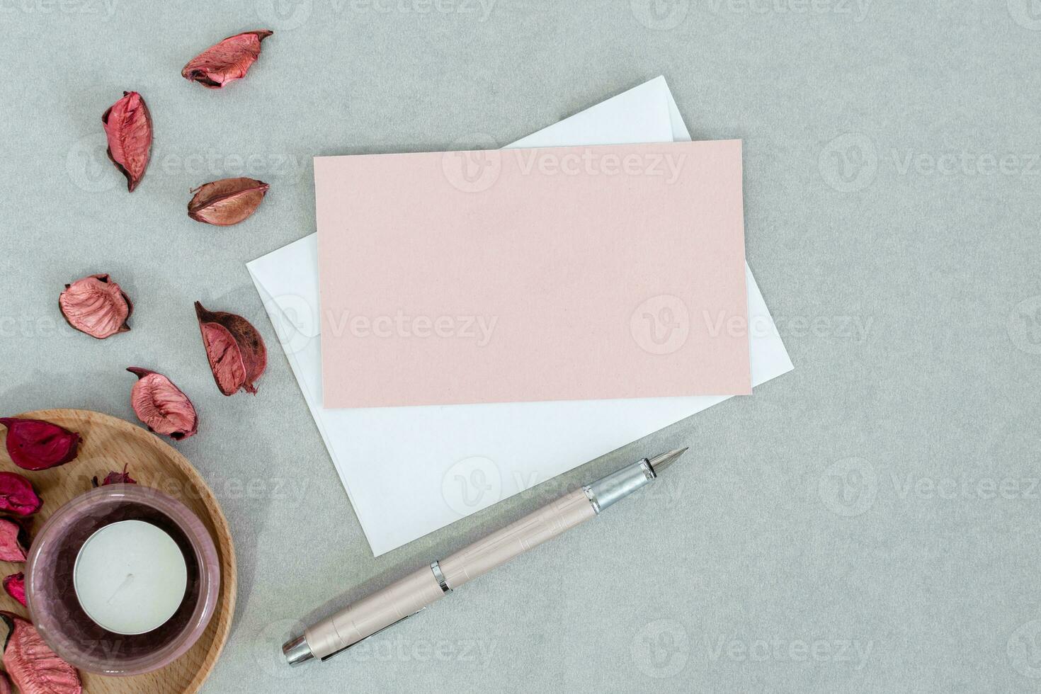 vide rose carte avec blanc enveloppe, bougie et pétales, sur gris Contexte. photo