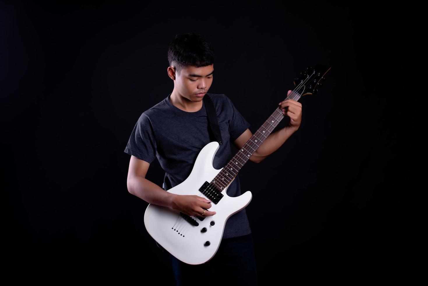 Jeune homme en veste de cuir noir avec guitare électrique sur fond noir en studio photo