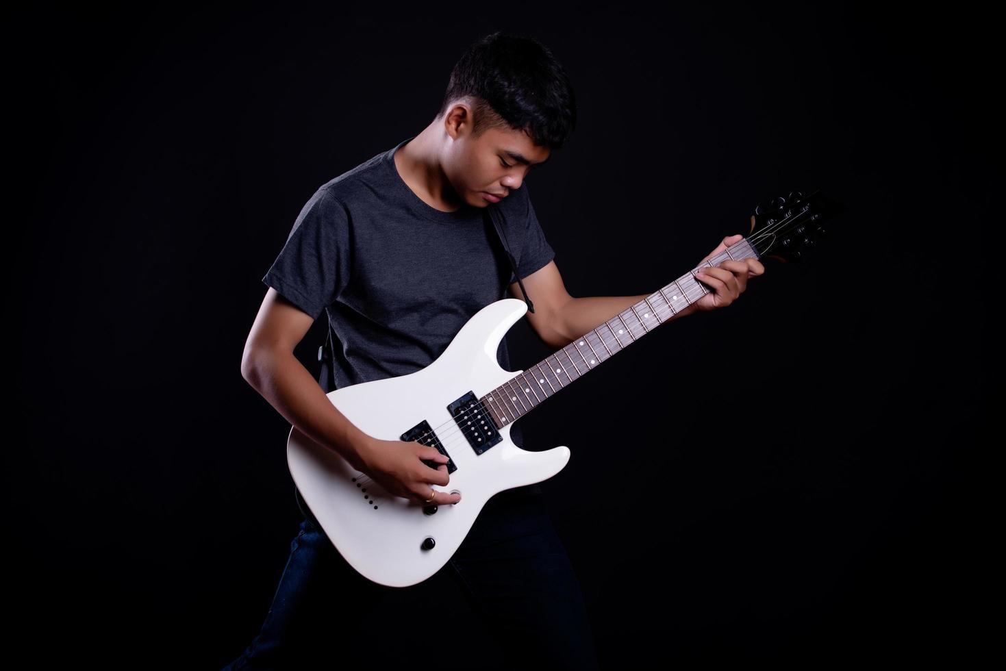 Jeune homme en veste de cuir noir avec guitare électrique sur fond noir en studio photo