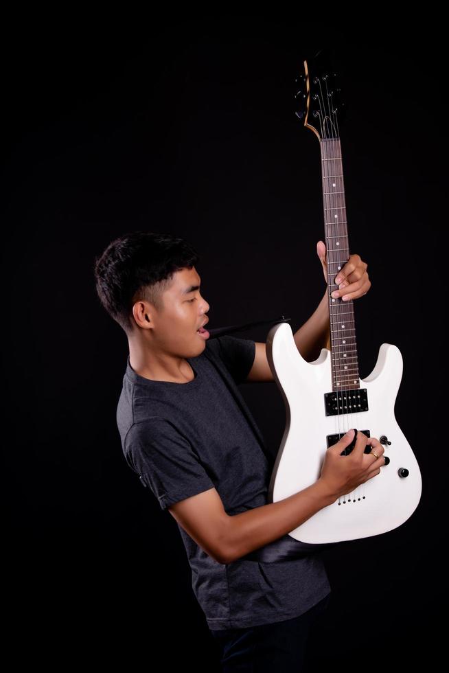 Jeune homme en veste de cuir noir avec guitare électrique sur fond noir en studio photo