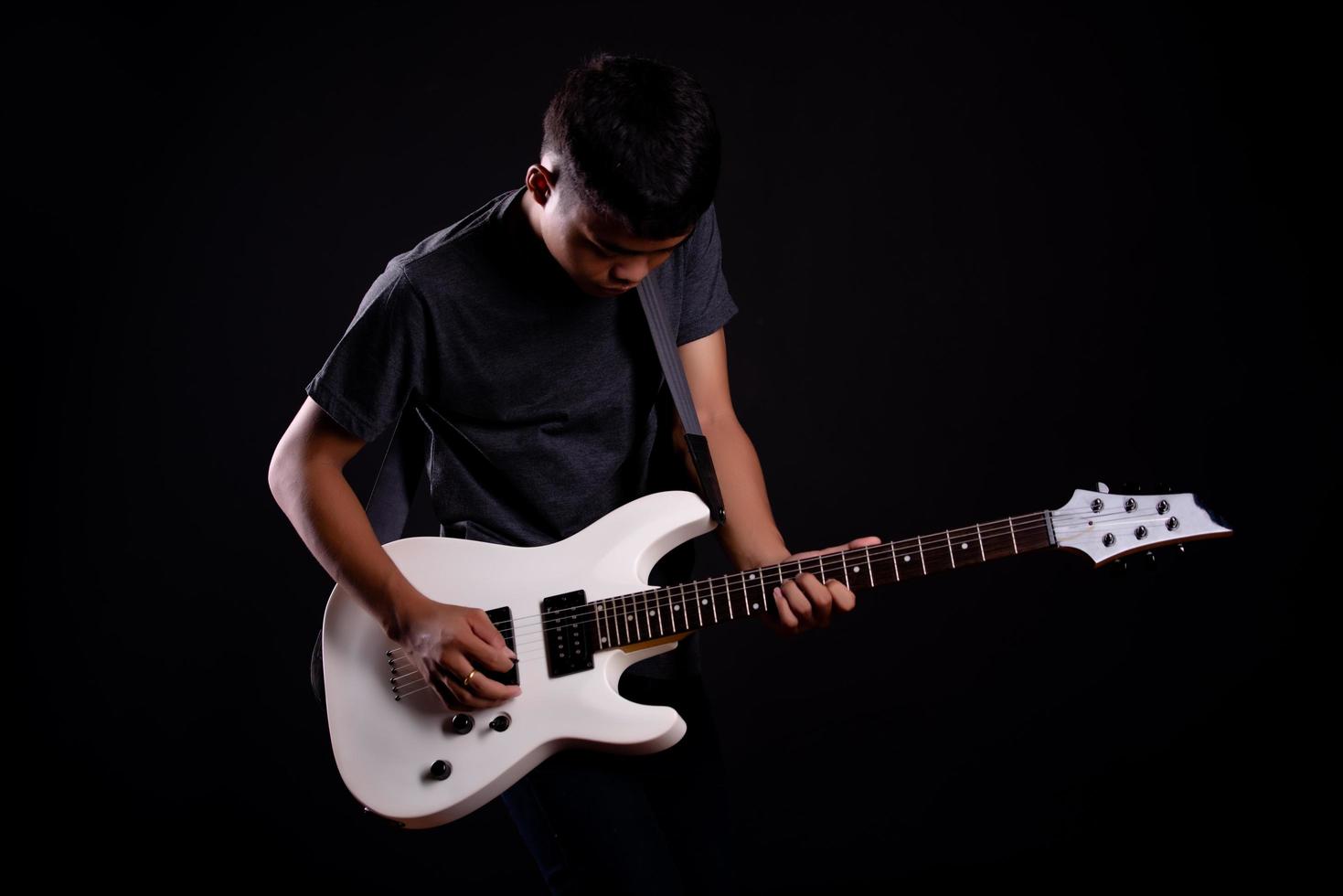 Jeune homme en blouson de cuir noir avec guitare électrique en studio photo