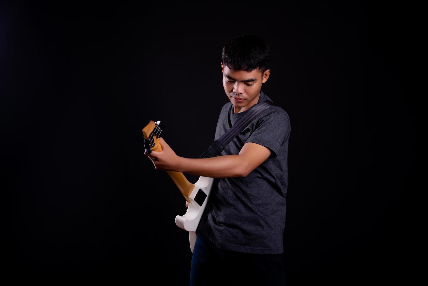 Jeune homme en veste de cuir noir avec guitare électrique sur fond noir en studio photo