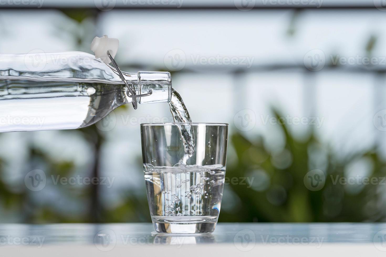 verser de l'eau potable de la bouteille dans le verre à la maison de jardin photo