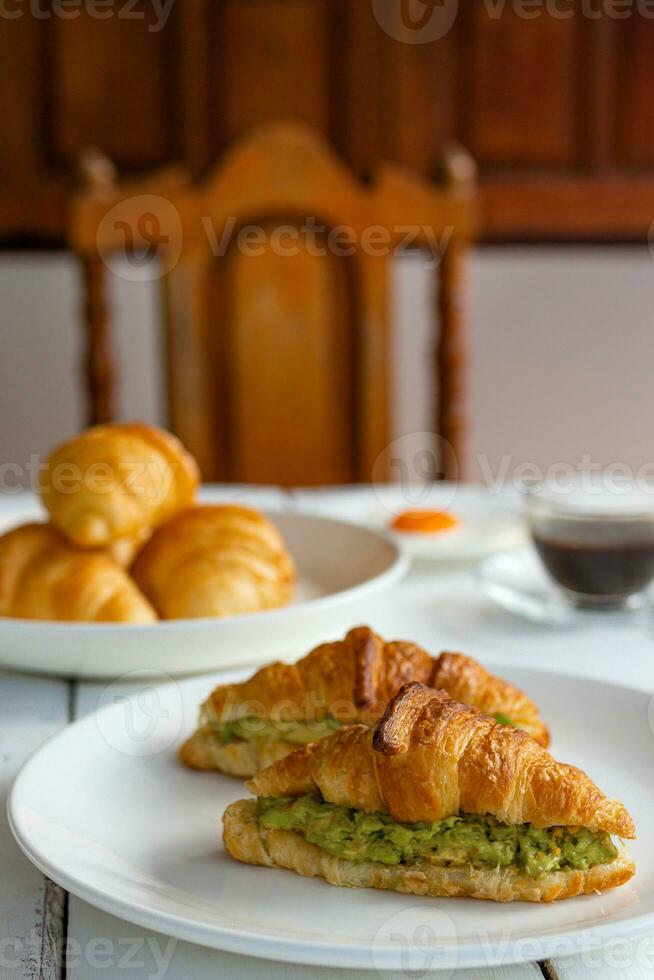 sandwich croissant avec oeuf, avocat sur plat blanc et miel, café. concept de petit-déjeuner et d'aliments sains. photo