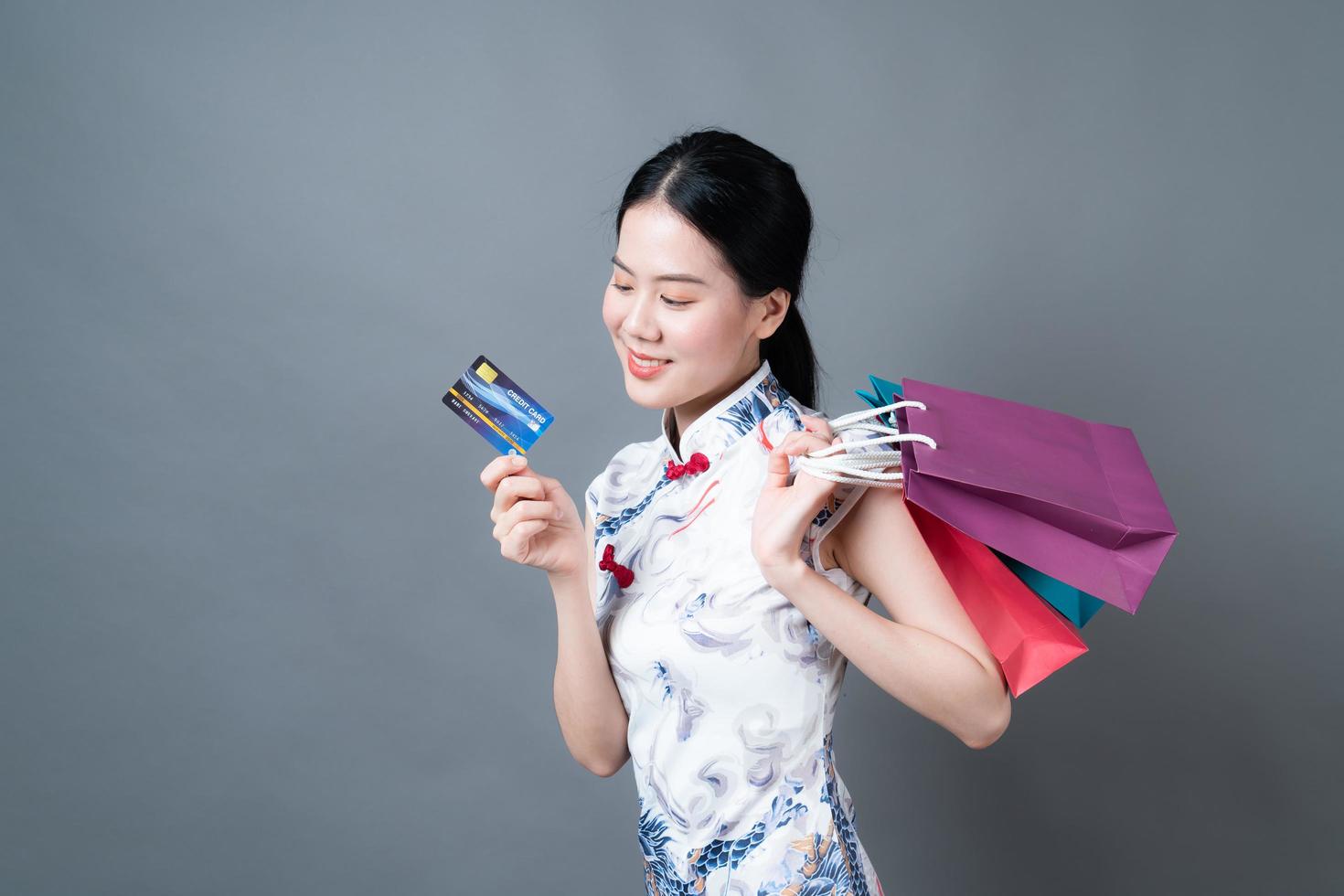 une femme asiatique porte une robe traditionnelle chinoise avec un sac à provisions et une carte de crédit photo