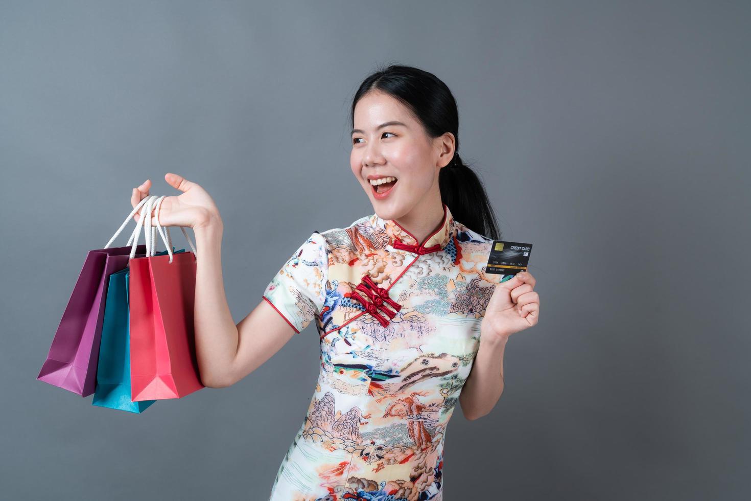 une femme asiatique porte une robe traditionnelle chinoise avec un sac à provisions et une carte de crédit photo