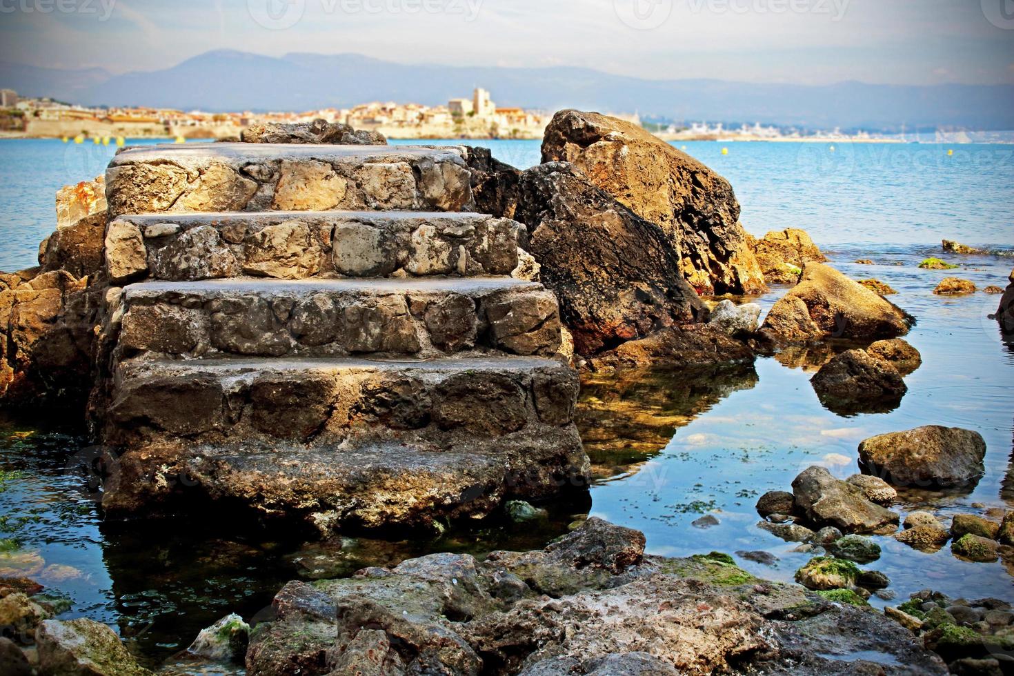 Ancien escalier en pierre de la tour isolé dans le fond bleu de l'eau de mer avec des rochers et des montagnes à l'horizon photo