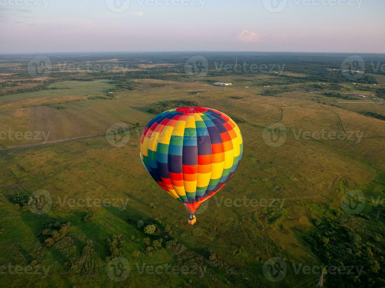 un ballon à air coloré vole en vol libre au-dessus du champ. vue à vol d'oiseau. ballon multicolore dans le ciel bleu photo