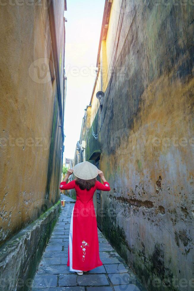 content femme portant ao dai vietnamien robe et chapeau, voyageur tourisme à salut un ancien ville dans central vietnam. point de repère et populaire pour touristique attractions. vietnam et sud-est Voyage concept photo