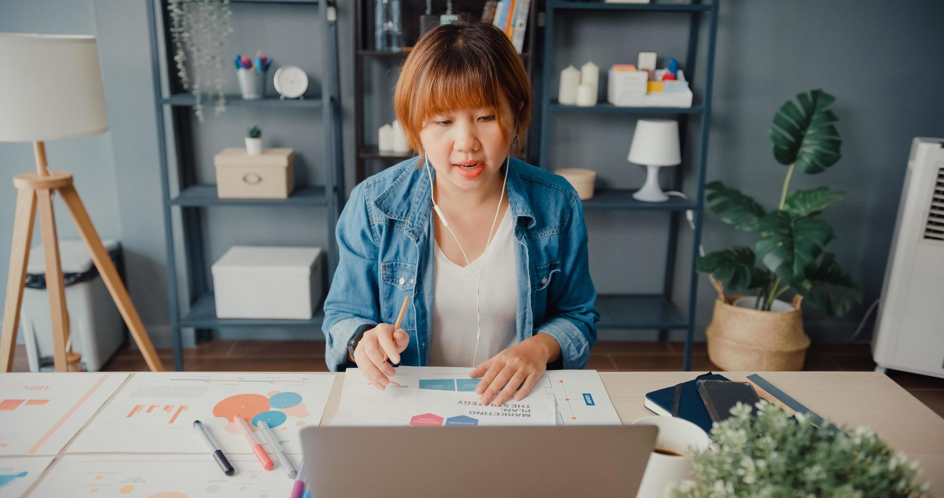 Une femme d'affaires asiatique utilisant un ordinateur portable parle à ses collègues du plan lors d'un appel vidéo tout en travaillant de la maison au salon photo