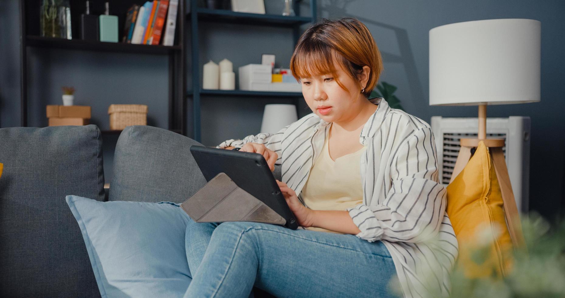 vêtements décontractés pour dames asiatiques indépendantes utilisant une tablette d'apprentissage en ligne dans le salon de la maison photo