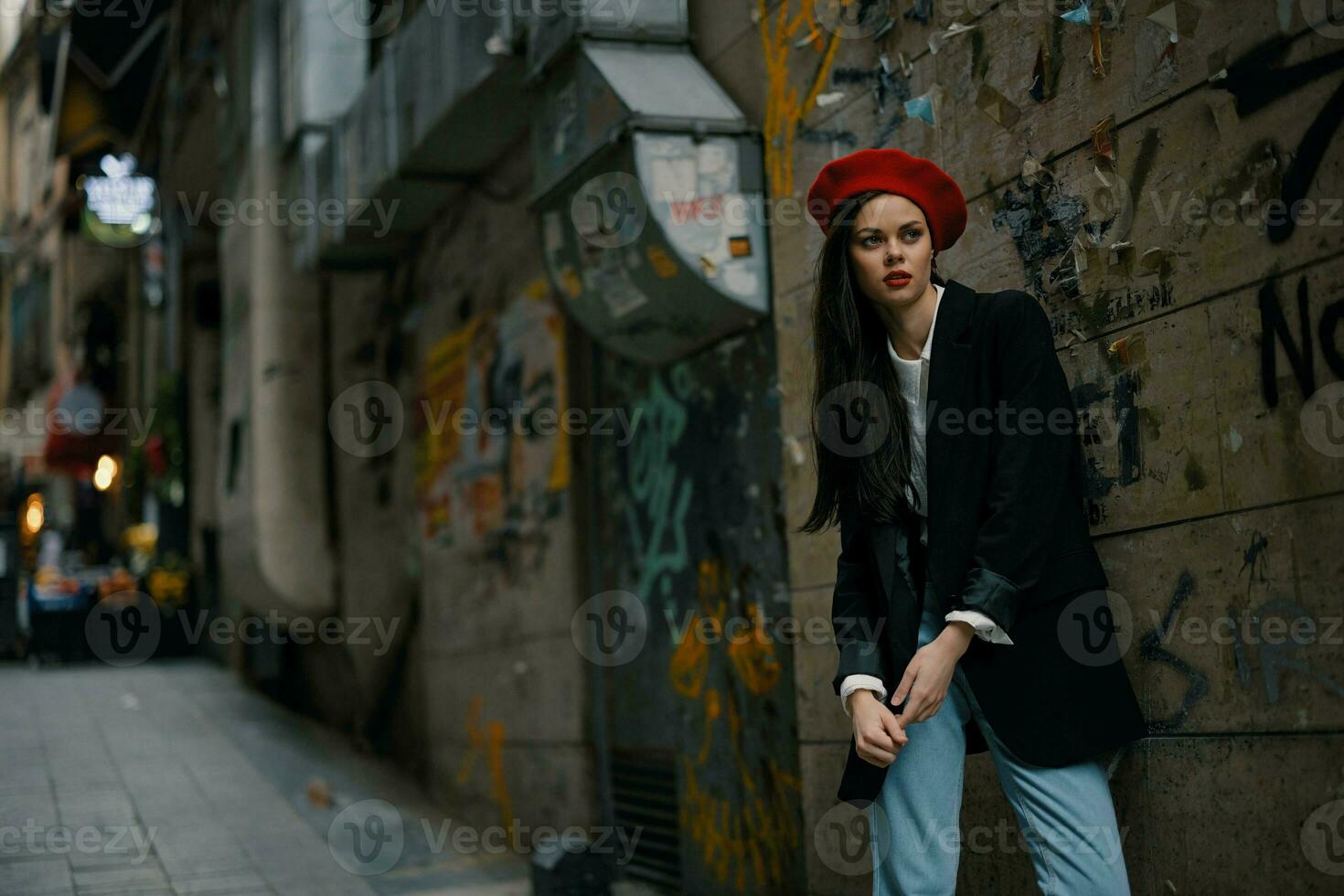 mode femme portrait en marchant touristique dans élégant vêtements avec rouge lèvres en marchant vers le bas une étroit ville rue, voyage, cinématique couleur, rétro ancien style, spectaculaire contre une mur avec graffiti. photo