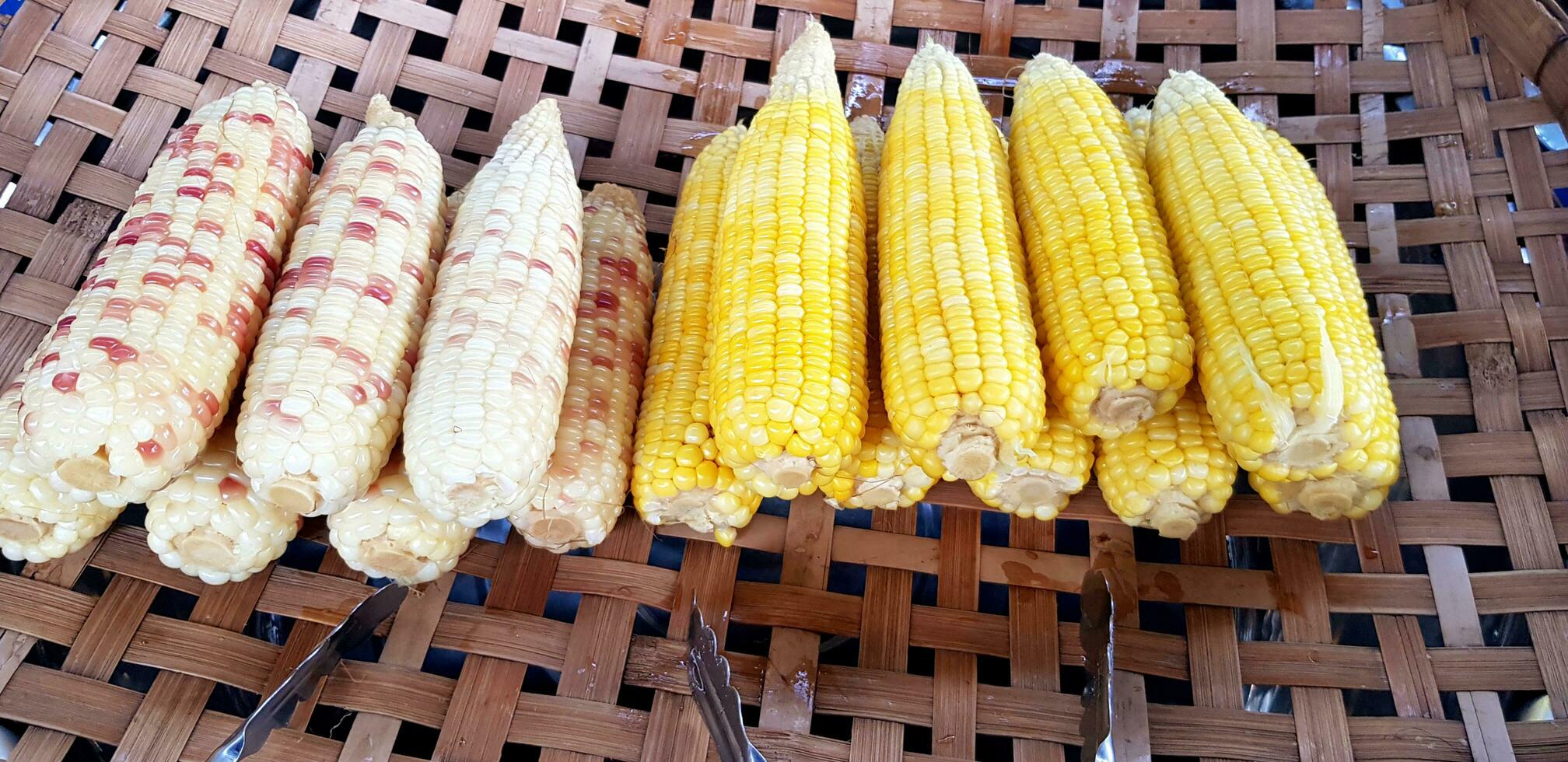 Frais à la vapeur blé avec inoxydable acier pinces sur bambou tisser plateau pour vente à rue nourriture marché. récolte de agriculture, en bonne santé ou régime nourriture et fraîcheur fruit concept photo