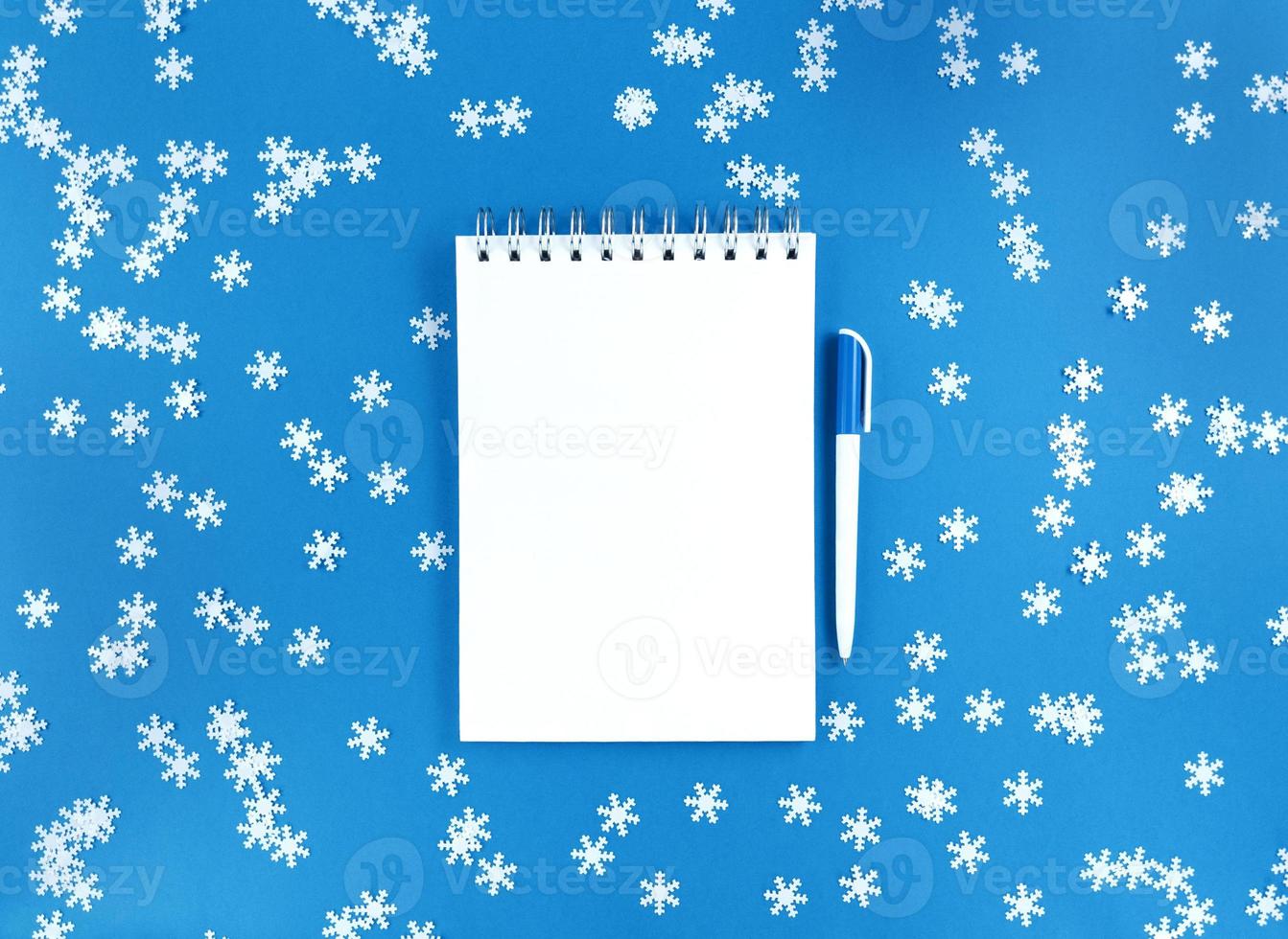 feuille de cahier vierge blanche et un stylo sur fond bleu avec des flocons de neige confettis épars. concept d'éducation de vacances. stock photo. photo