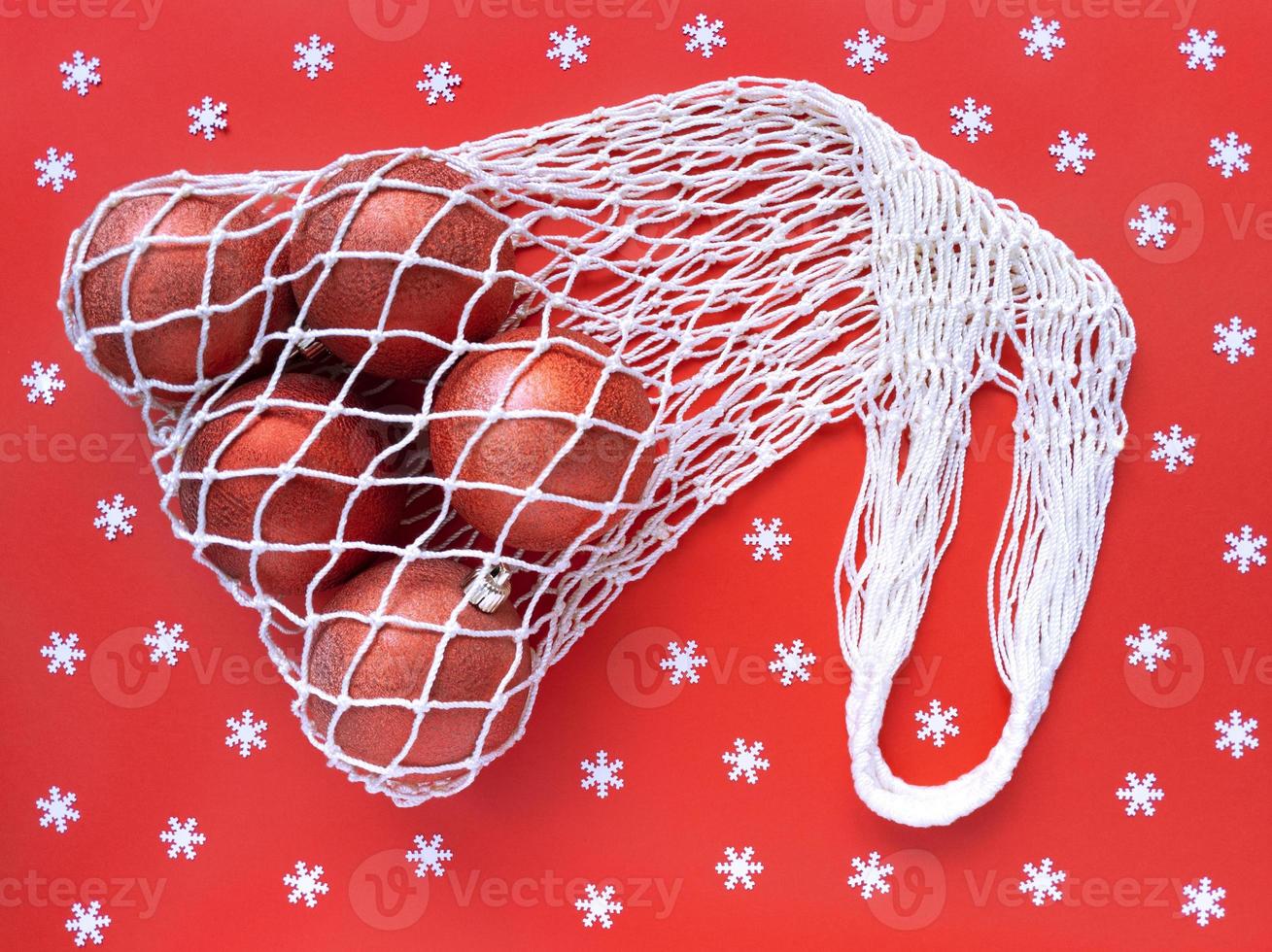 sac écologique en coton à ficelle blanche avec cinq boules d'arbre de Noël sur fond rouge et flocons de neige blancs dispersés. vacances simple mise à plat. concept écologique zéro déchet. stock photo. photo