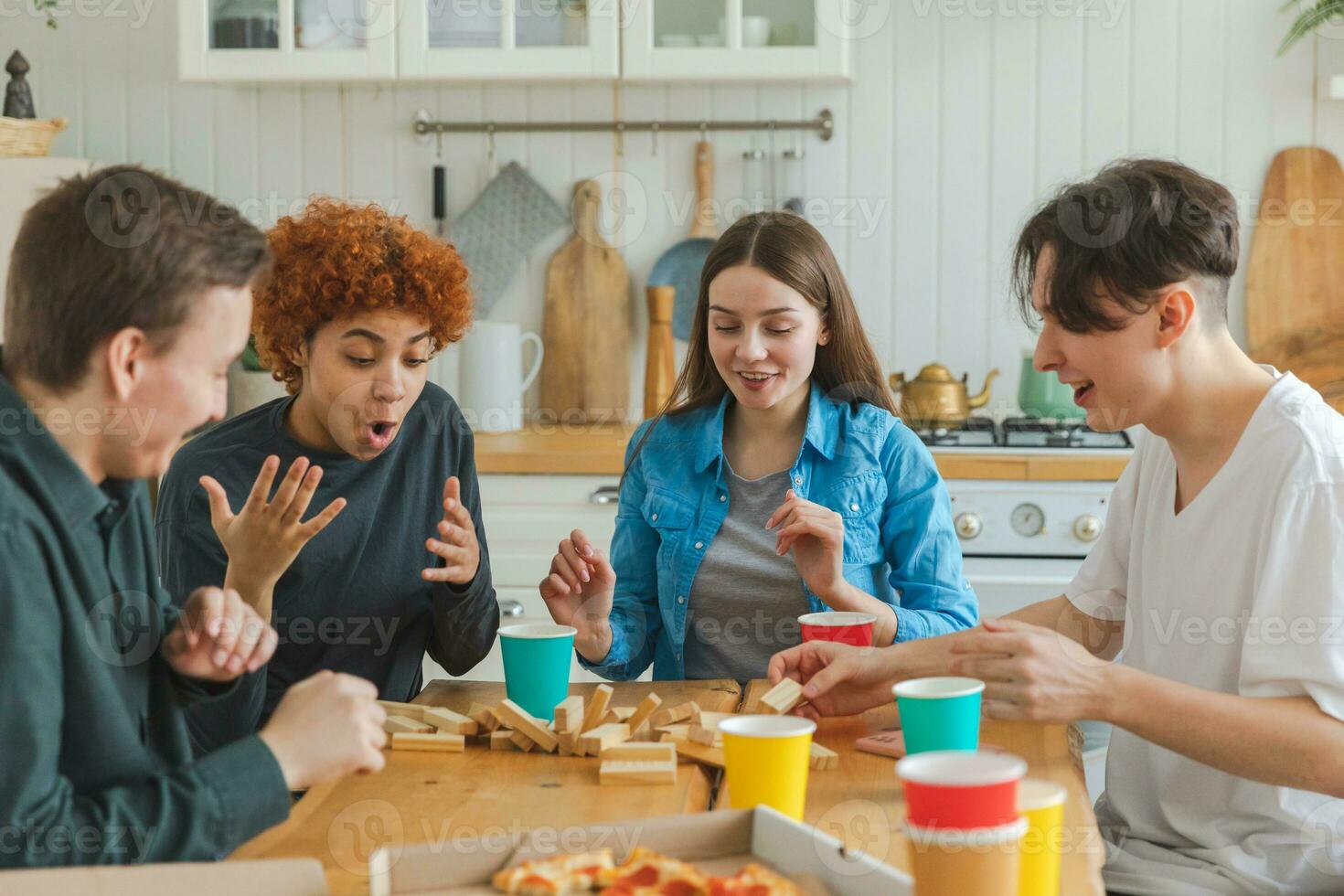 Accueil faire la fête. copains dépenses temps ensemble en jouant dans planche Jeu crash en bois la tour à maison. content diverse groupe ayant amusement ensemble intérieur. mixte course Jeune copains meilleur copains profiter fin de semaine. photo