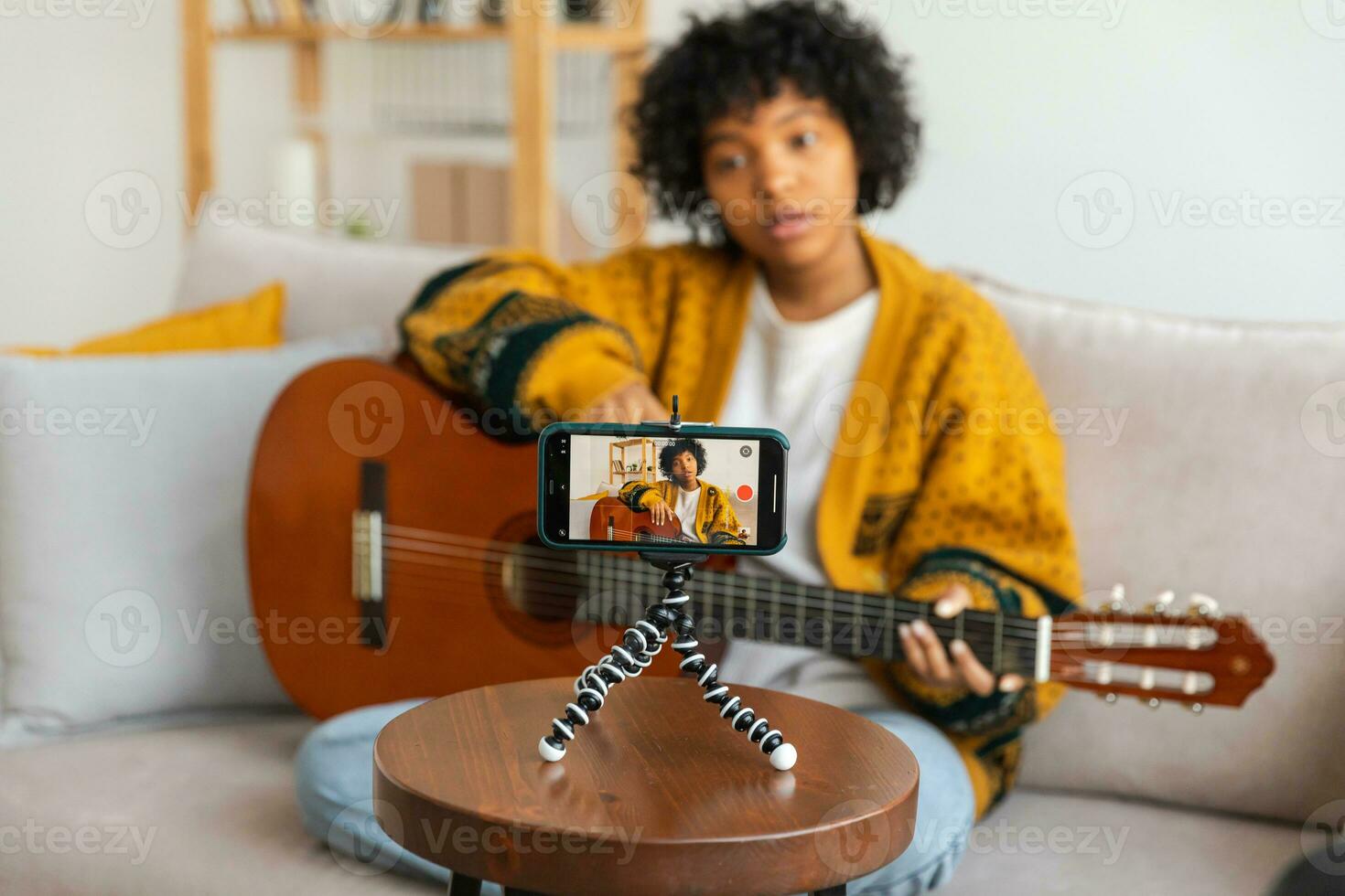 blogueur guitariste. africain américain fille blogueur en jouant guitare parlant à webcam enregistrement vlog. social médias influenceur femme diffusion à Accueil à l'intérieur. la musique contenu créateur diffuser Didacticiel. photo