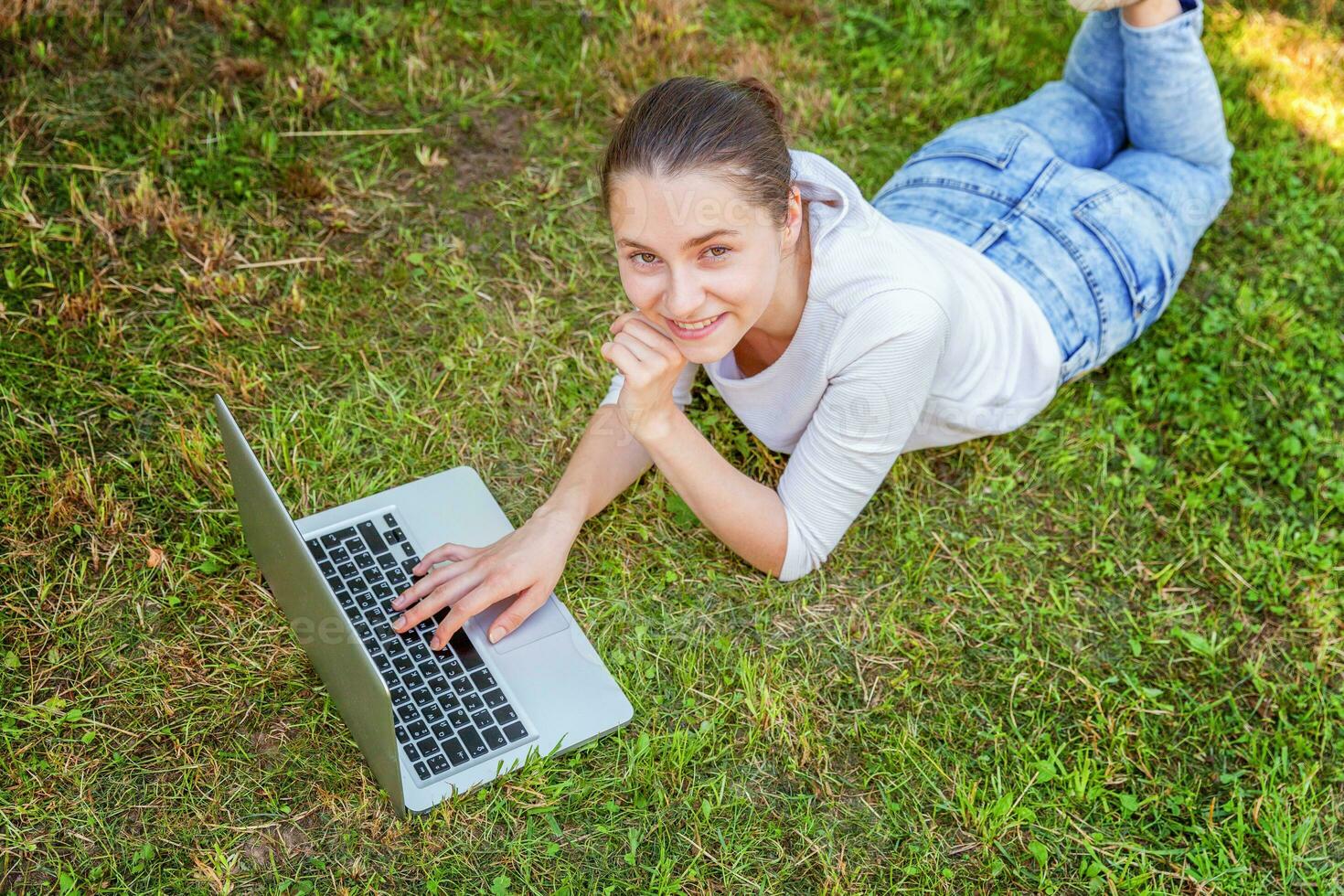 Jeune femme mensonge sur vert herbe pelouse dans ville parc travail sur portable PC ordinateur. free-lance affaires concept photo