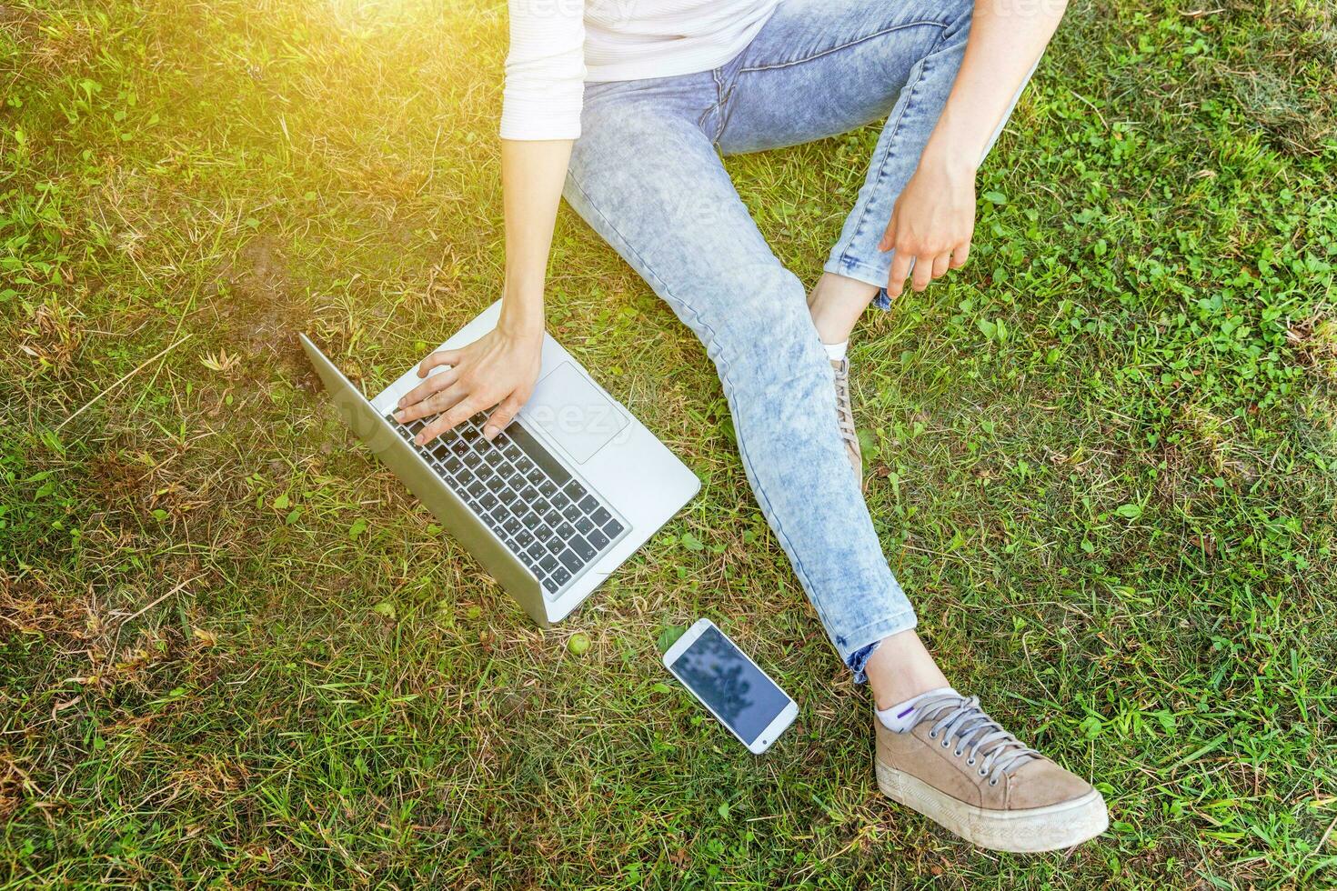 jambes de femme sur la pelouse d'herbe verte dans le parc de la ville, mains travaillant sur un ordinateur portable. concept d'entreprise indépendant photo