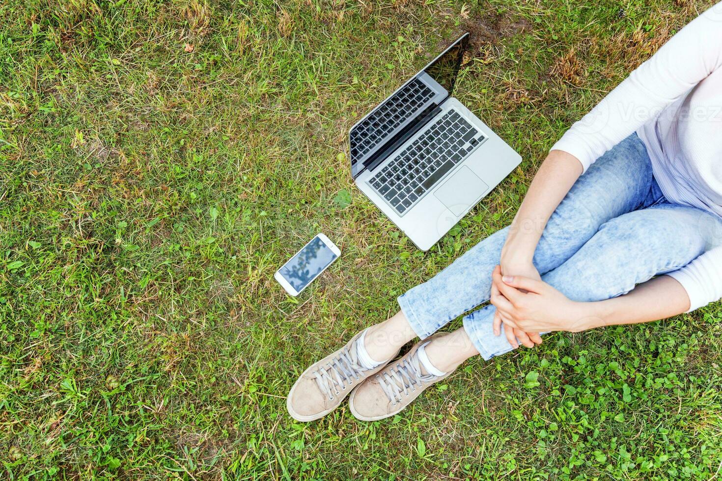 jambes de femme sur la pelouse d'herbe verte dans le parc de la ville, mains travaillant sur un ordinateur portable. concept d'entreprise indépendant photo