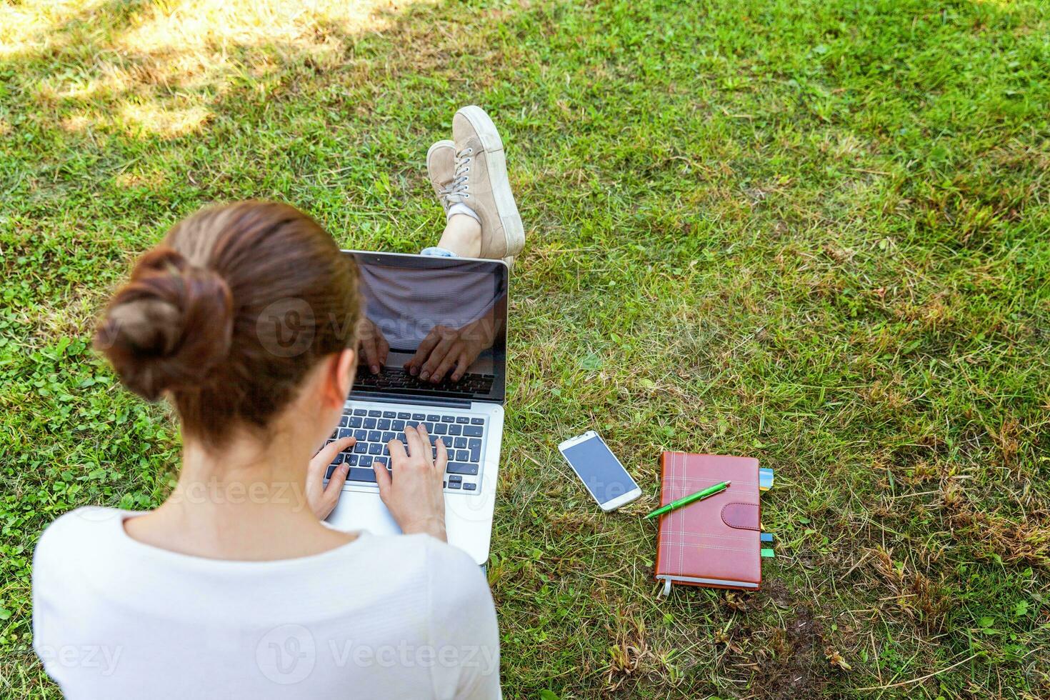 jeune femme assise sur une pelouse d'herbe verte dans le parc de la ville travaillant sur un ordinateur portable. concept d'entreprise indépendant photo