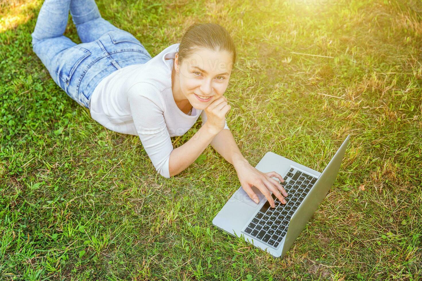 Jeune femme mensonge sur vert herbe pelouse dans ville parc travail sur portable PC ordinateur. free-lance affaires concept photo