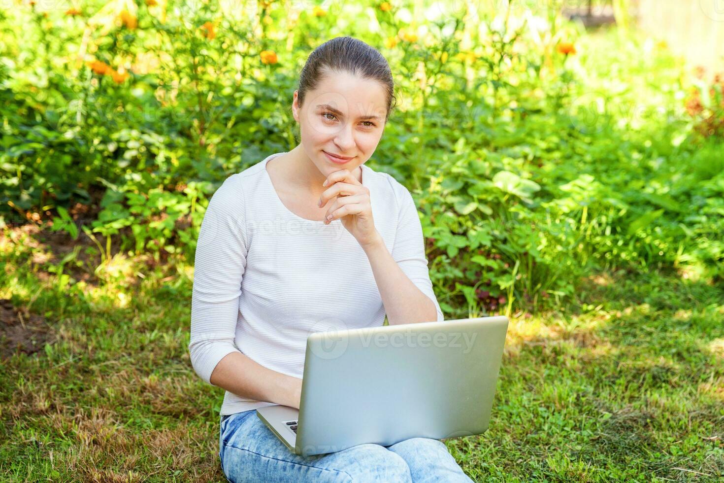 jeune femme assise sur une pelouse d'herbe verte dans le parc de la ville travaillant sur un ordinateur portable. concept d'entreprise indépendant photo