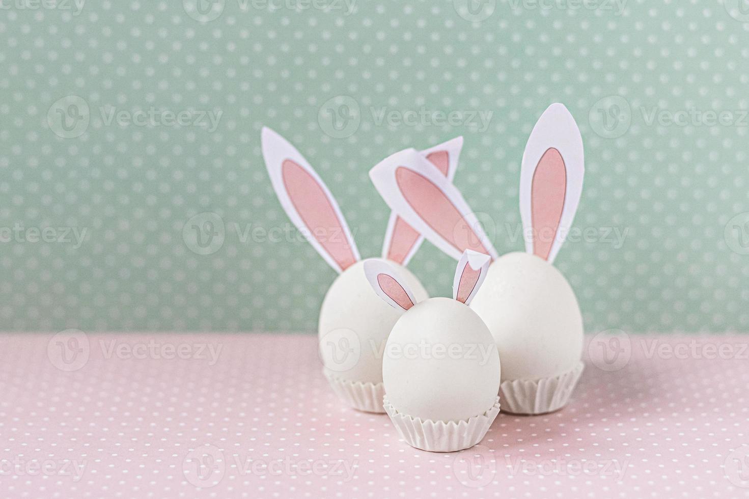 oeufs de poule blancs avec des oreilles et des queues de lapin sur fond de fleurs de lit. une famille. concept de joyeuses fêtes de pâques photo