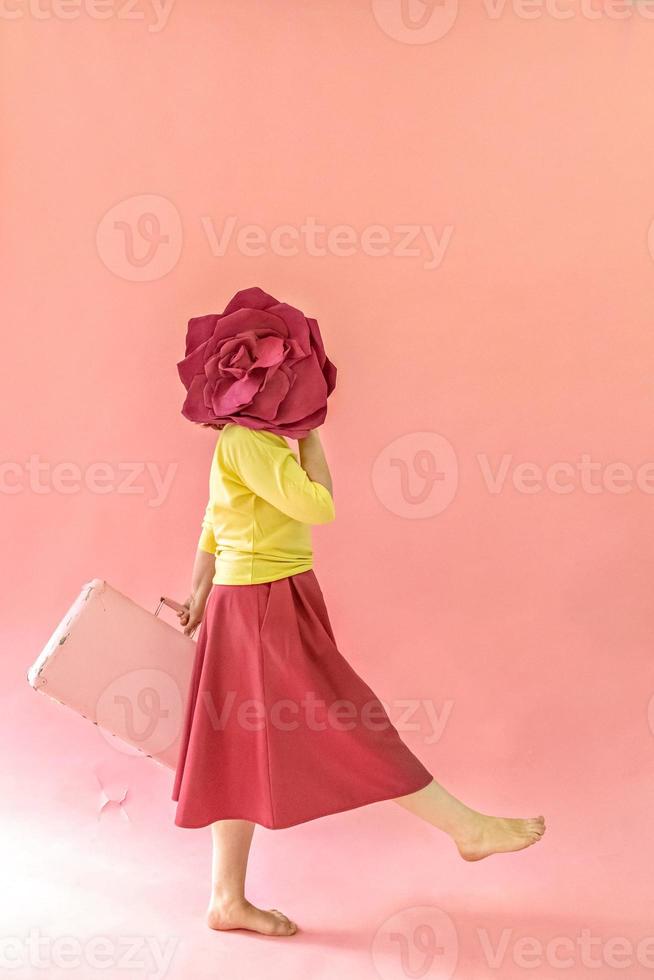 une jeune femme avec une valise dans les mains et une fleur sur fond rose. le concept de voyage dans la pandémie de coronavirus photo