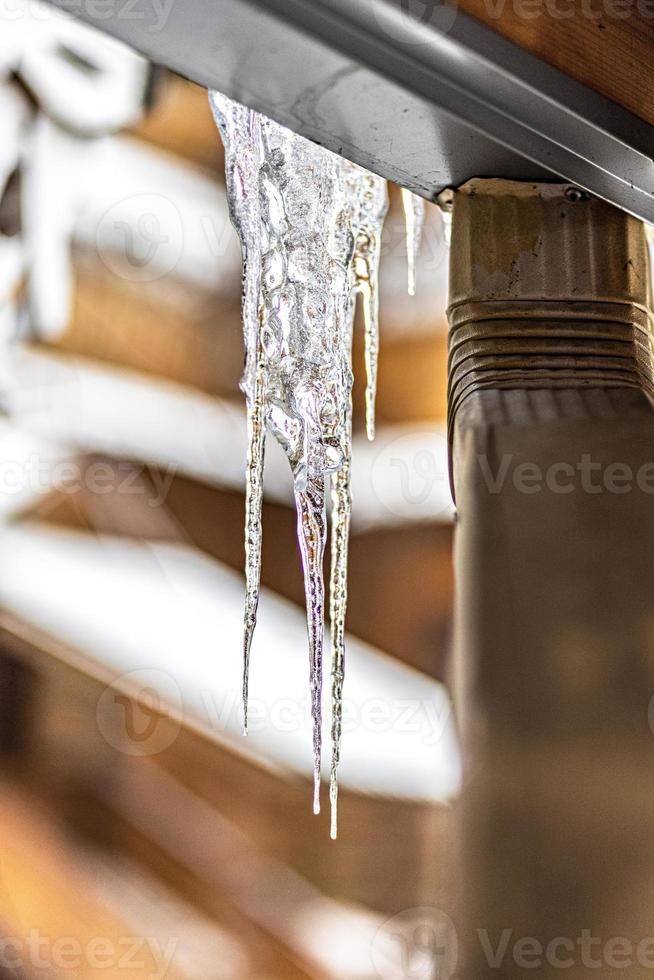 un gros glaçon de glace transparent est suspendu au toit de la maison. gelées d'hiver photo