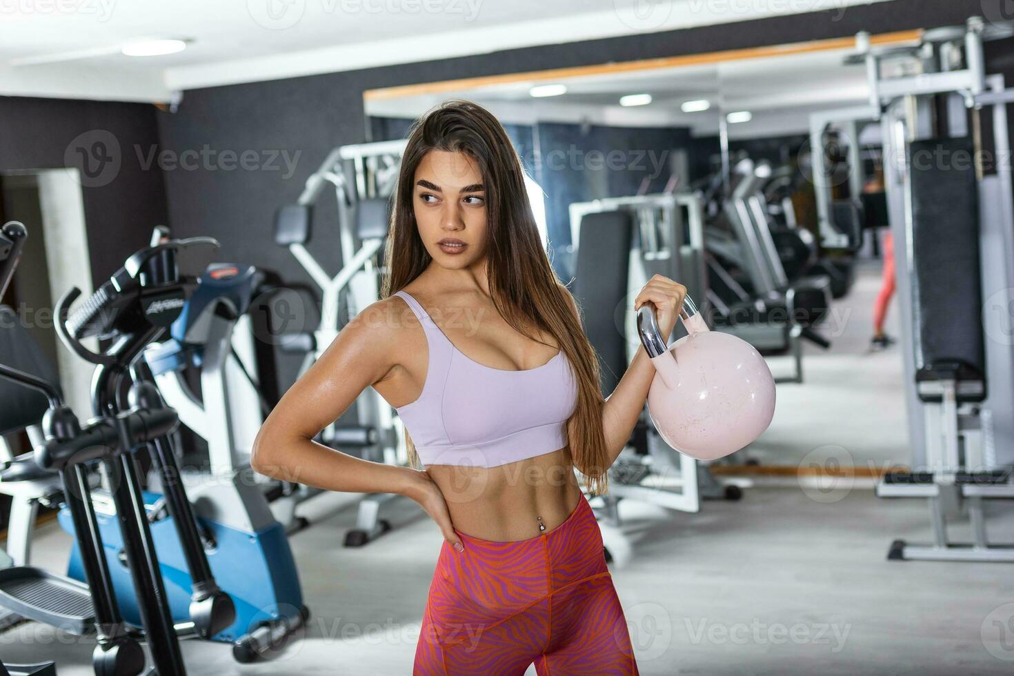 attrayant Jeune athlète avec musclé corps exercice cross-fit. femme dans tenue de sport Faire crossfit faire des exercices avec bouilloire cloche photo