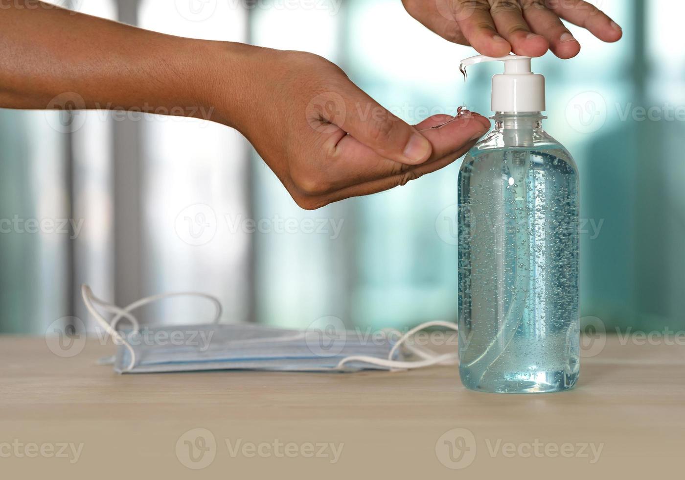 main avec désinfectant pour les mains au gel d'alcool et masque médical sur table photo