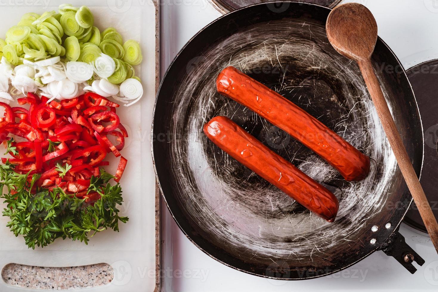 saucisse frite sur poêle rustique, mélange de légumes frais, poivrons, persil et poireau sur panneau de cuisine prêt à être frit. photo
