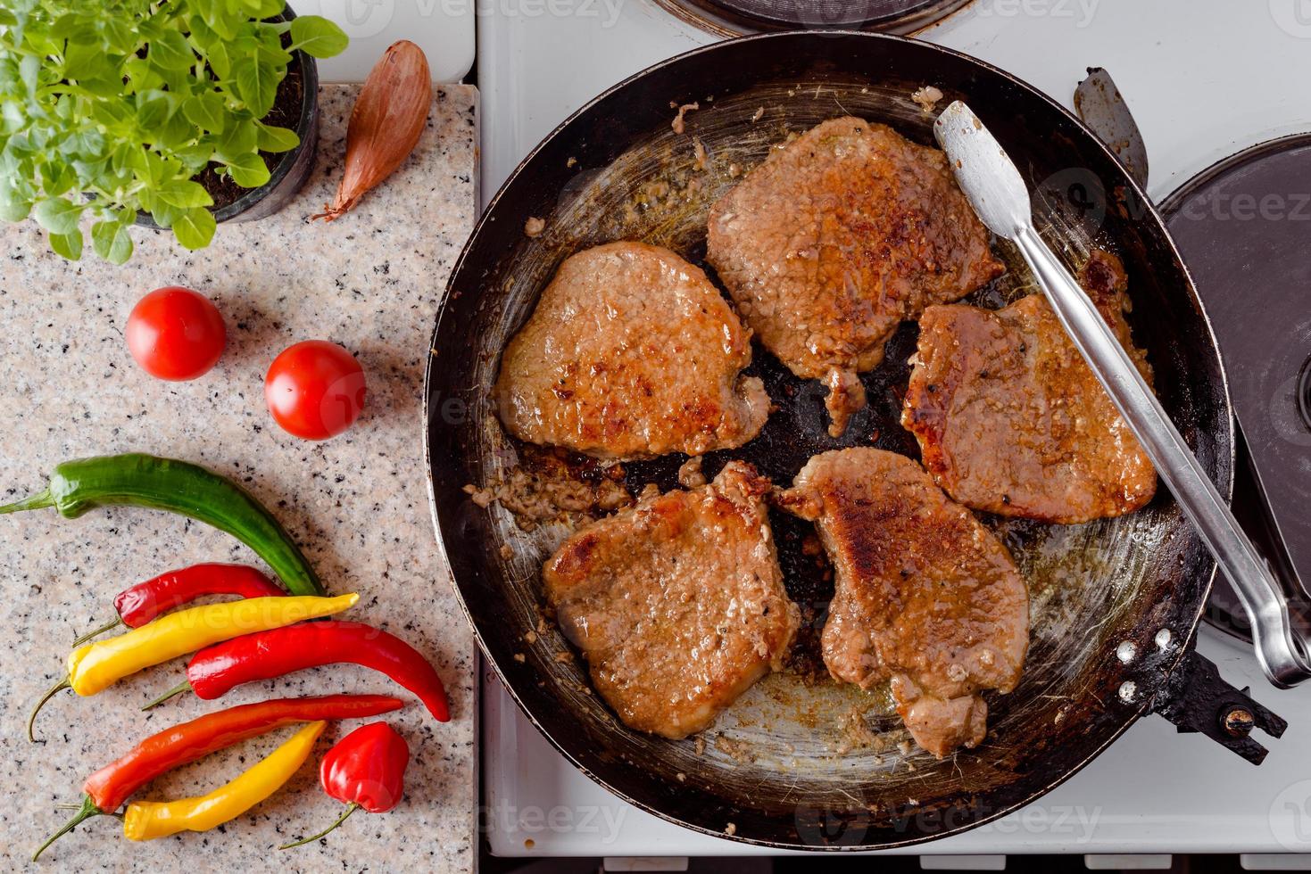 steak de porc rôti sur une poêle rustique, piments forts frais, tomates et herbes. photo