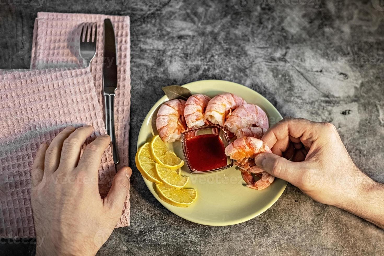 la main d'un homme tient une crevette royale. sur une assiette de crevettes, sauce aux airelles et citron.le concept d'une alimentation saine photo
