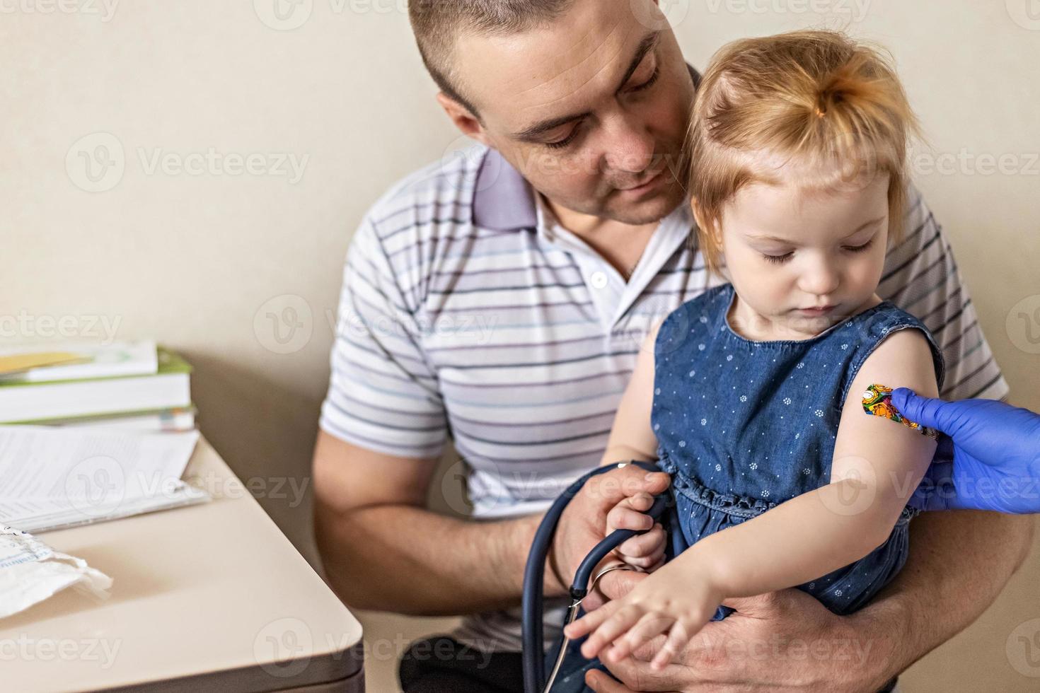 vaccination d'une petite fille dans les bras de son père dans le cabinet du médecin contre le coronavirus. pansement adhésif amusant pour enfants. vaccin contre covid-19, grippe, maladies infectieuses. photo