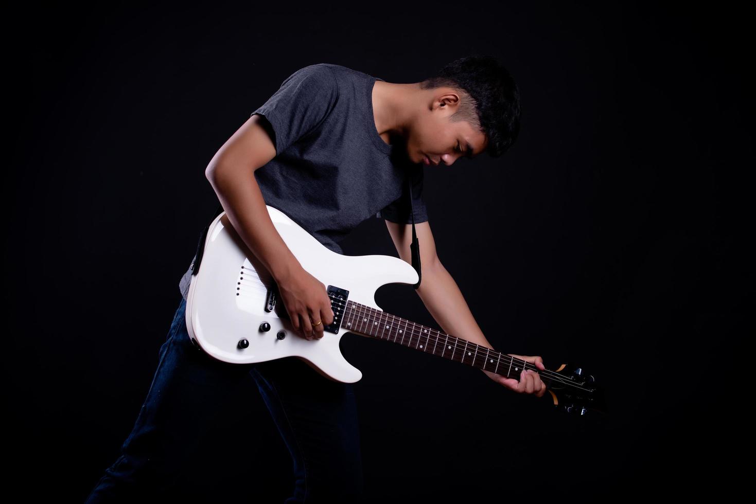 Jeune homme en blouson de cuir noir avec guitare électrique en studio photo