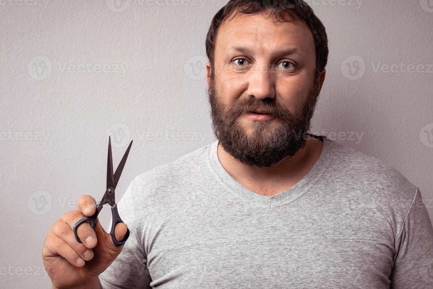 bel homme barbu en t-shirt gris tenant des ciseaux sur fond gris. photo