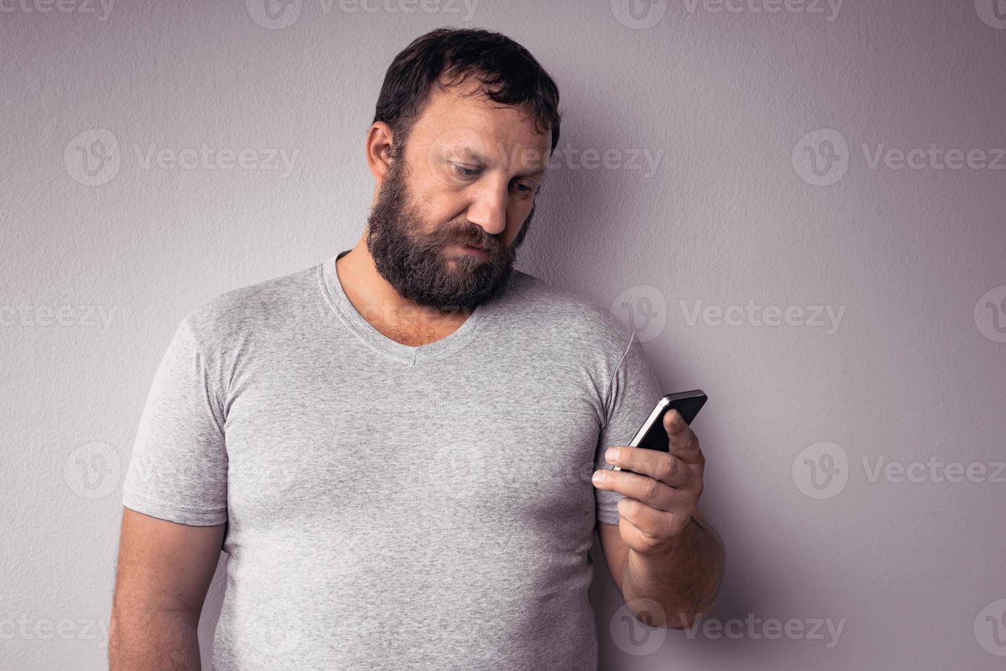 homme barbu en t-shirt gris tenant un téléphone portable photo