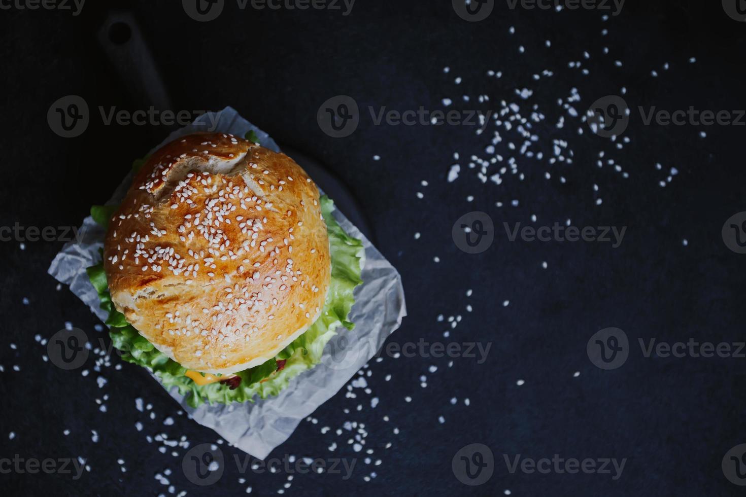 appétissant burger frais fait maison, avec escalope de poulet, laitue, tomates, fromage et sauce. sur une planche de bois sur fond noir photo