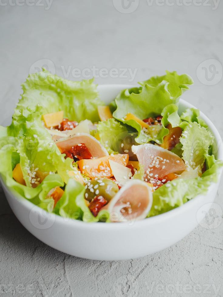 salade fraîche de laitue, tomates cerises, olives, tomates séchées, jambon de parme, cheddar, parmesan, huile d'olive et sésame. concept d'alimentation saine. photo