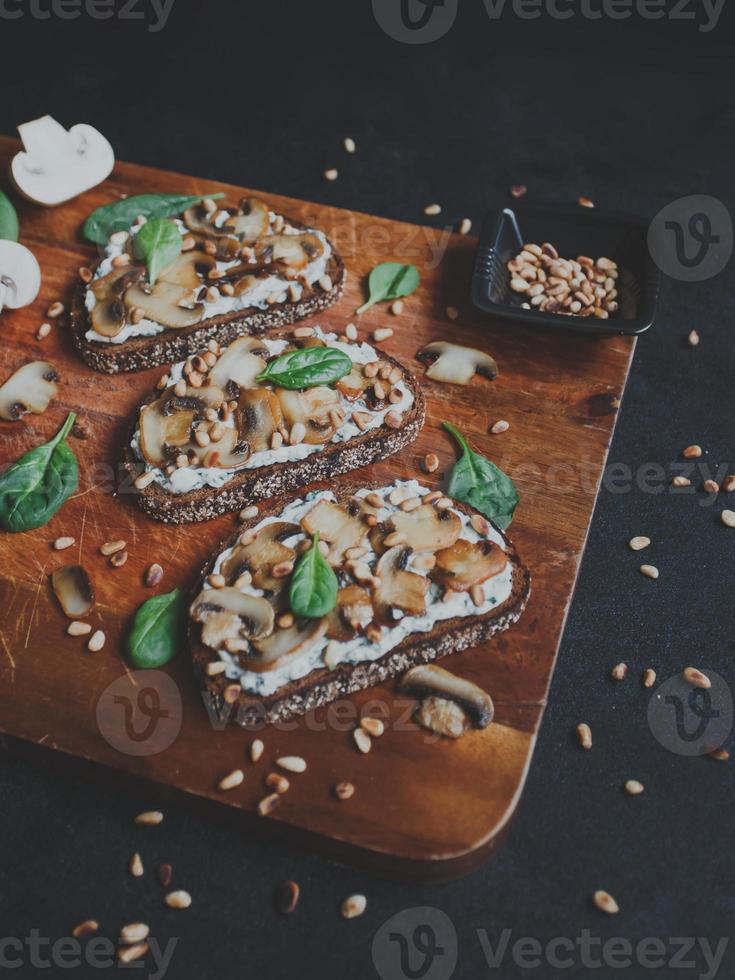 savoureuse bruschetta fraîche aux champignons, épinards, ail, fromage à la crème et pignons, sur une planche de bois, sur fond sombre. photo