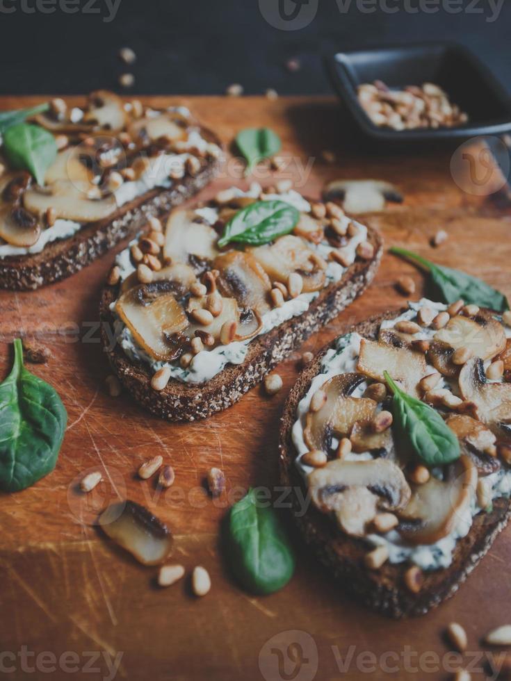 savoureuse bruschetta fraîche aux champignons, épinards, ail, fromage à la crème et pignons, sur une planche de bois, sur fond sombre. photo