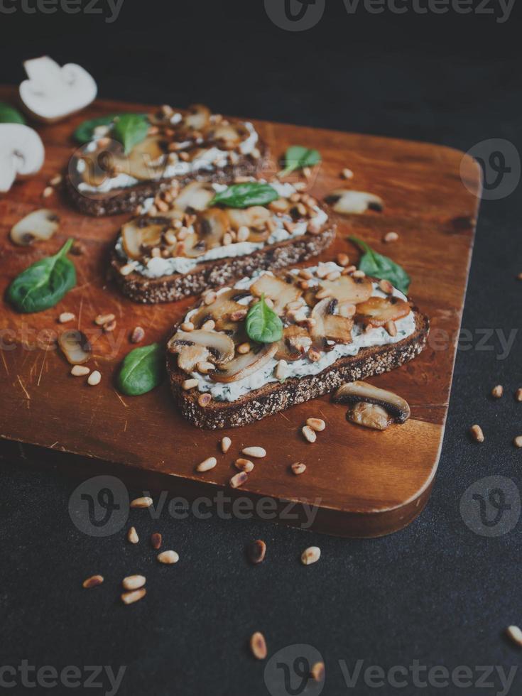 savoureuse bruschetta fraîche aux champignons, épinards, ail, fromage à la crème et pignons, sur une planche de bois, sur fond sombre. photo