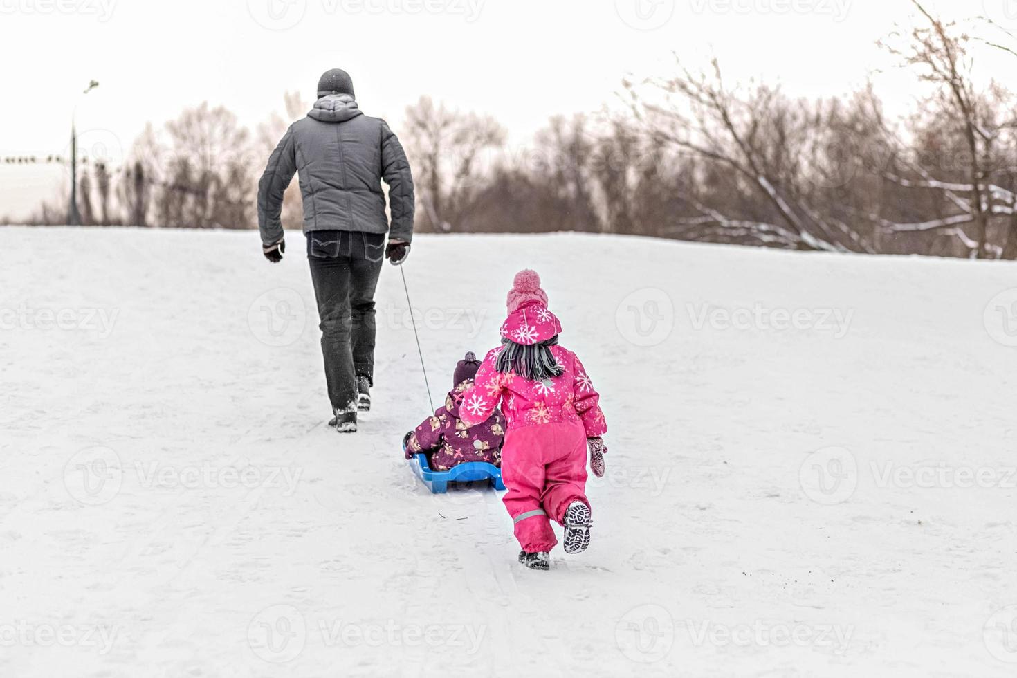 papa et ses deux enfants jouent et font de la luge dans le parc. photo