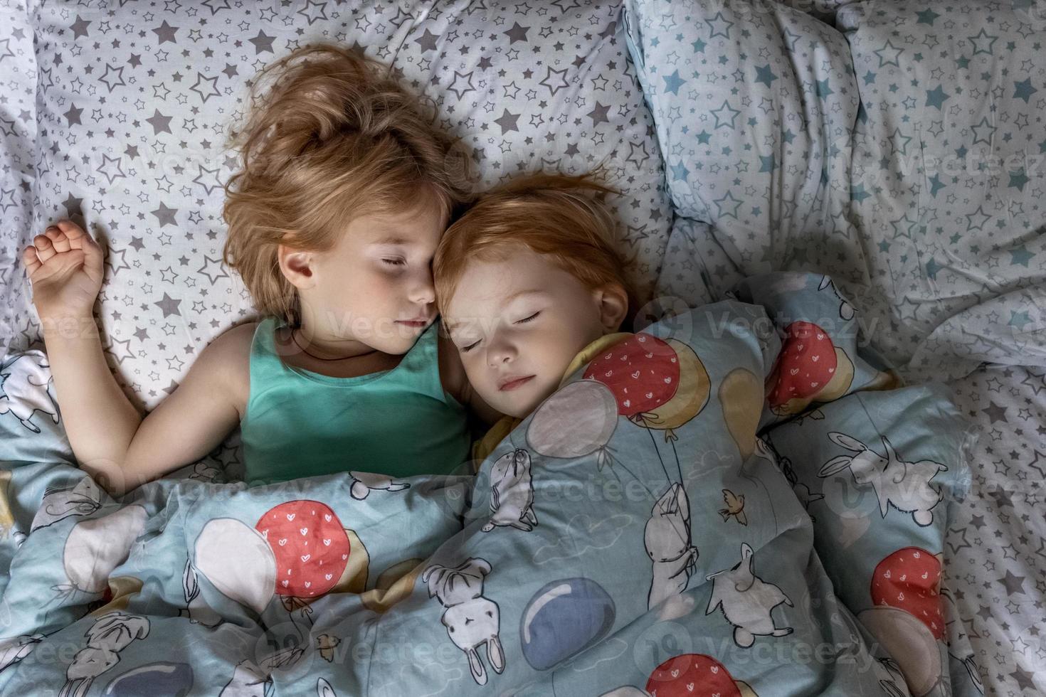 Deux petites sœurs filles sœurs dormant dans une étreinte au lit sous une couverture photo
