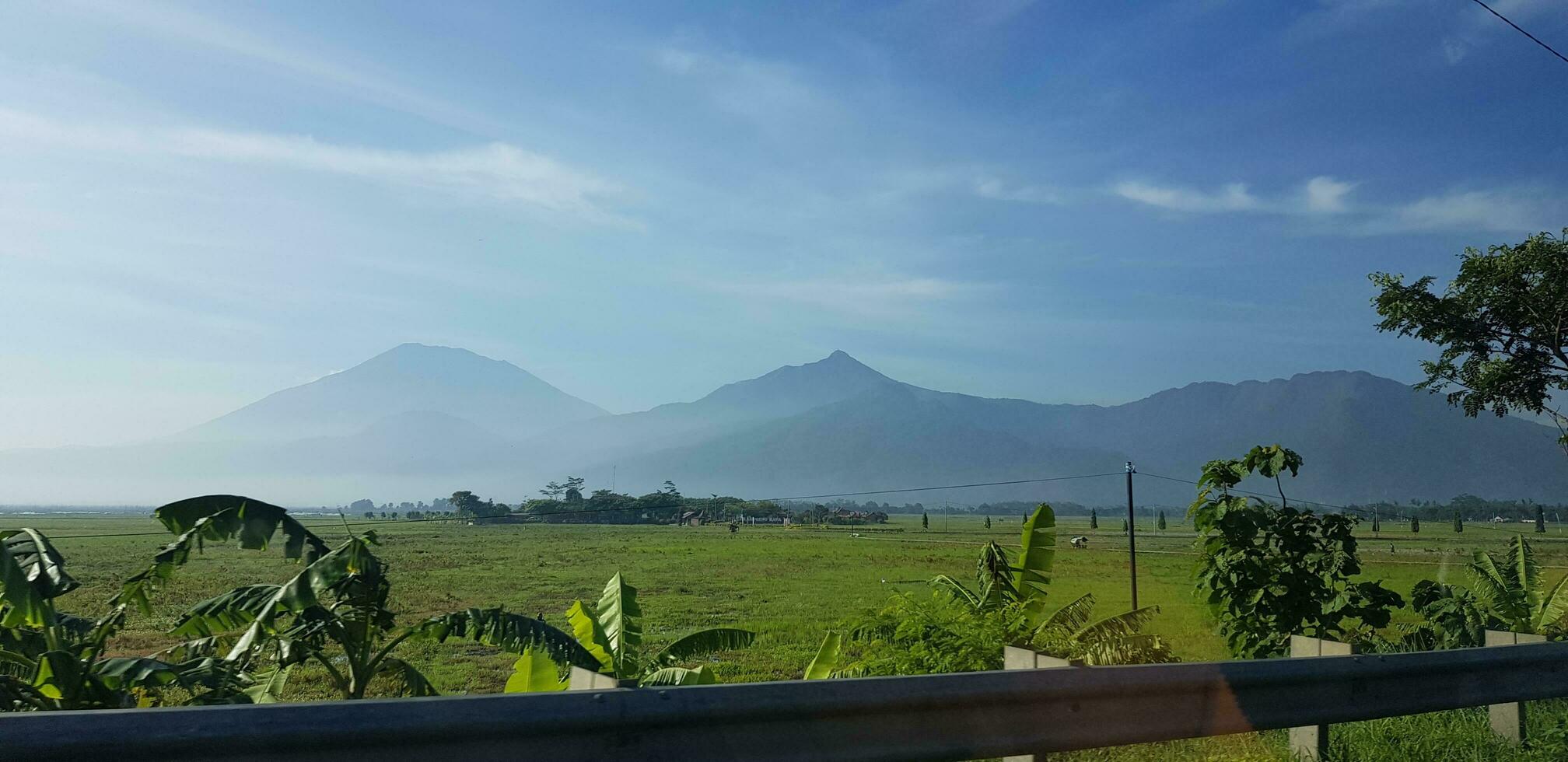 une vue de vert riz des champs et jardins avec bleu ciel et blanc des nuages et le silhouette de une Montagne photo