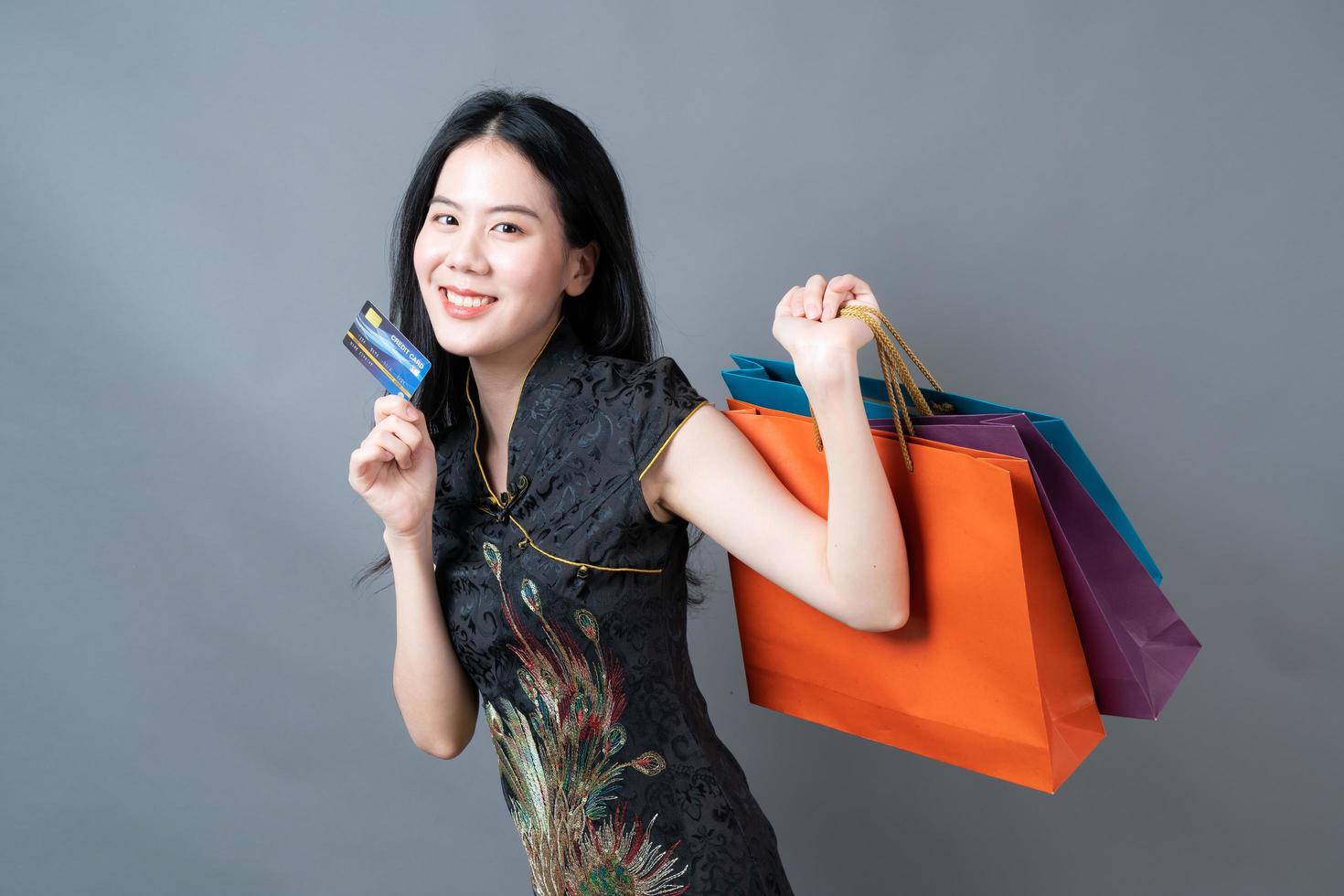 une femme asiatique porte une robe traditionnelle chinoise avec un sac à provisions et une carte de crédit photo