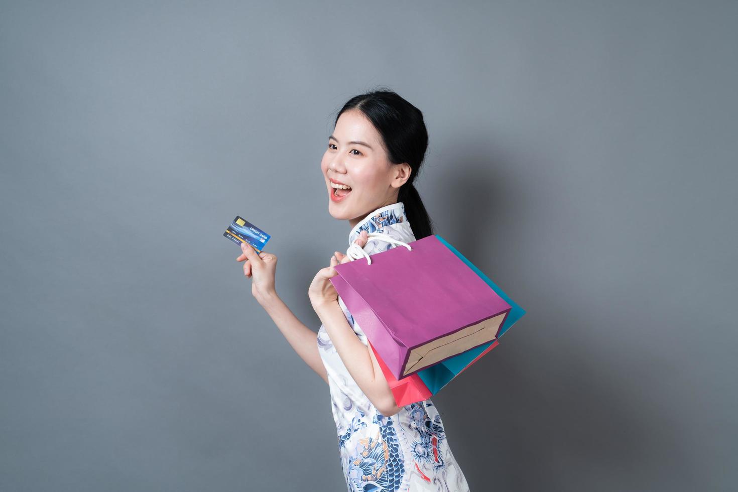 une femme asiatique porte une robe traditionnelle chinoise avec un sac à provisions et une carte de crédit photo