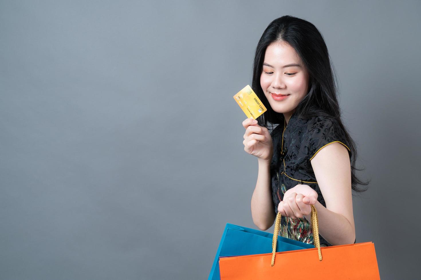 une femme asiatique porte une robe traditionnelle chinoise avec un sac à provisions et une carte de crédit photo